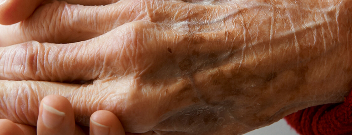 Eine ältere Hand wird sanft von einer anderen Hand gehalten.